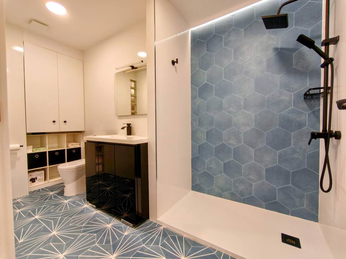 Baño reformado con ducha a ras de suelo, azulejo hexagonal azul y grifería negra