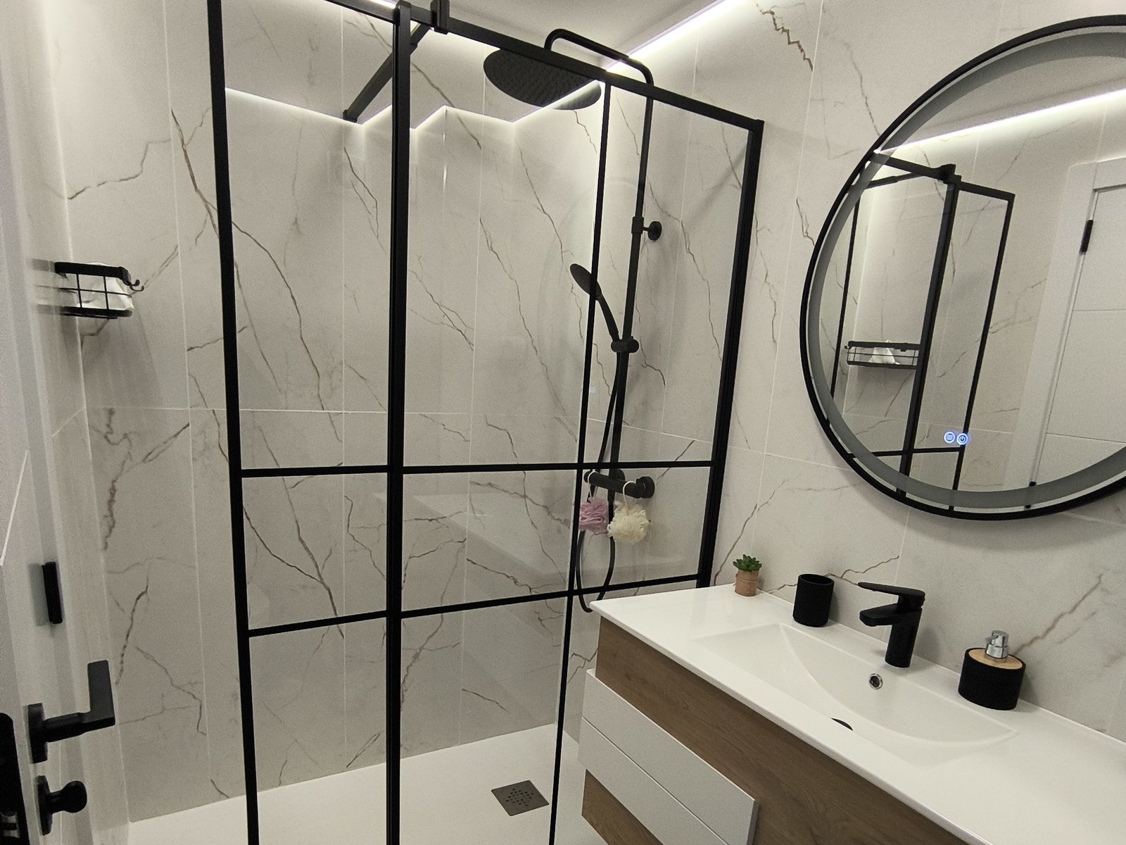 Ducha a ras de suelo con mampara de perfil negro y azulejo tipo mármol, tras la reforma
