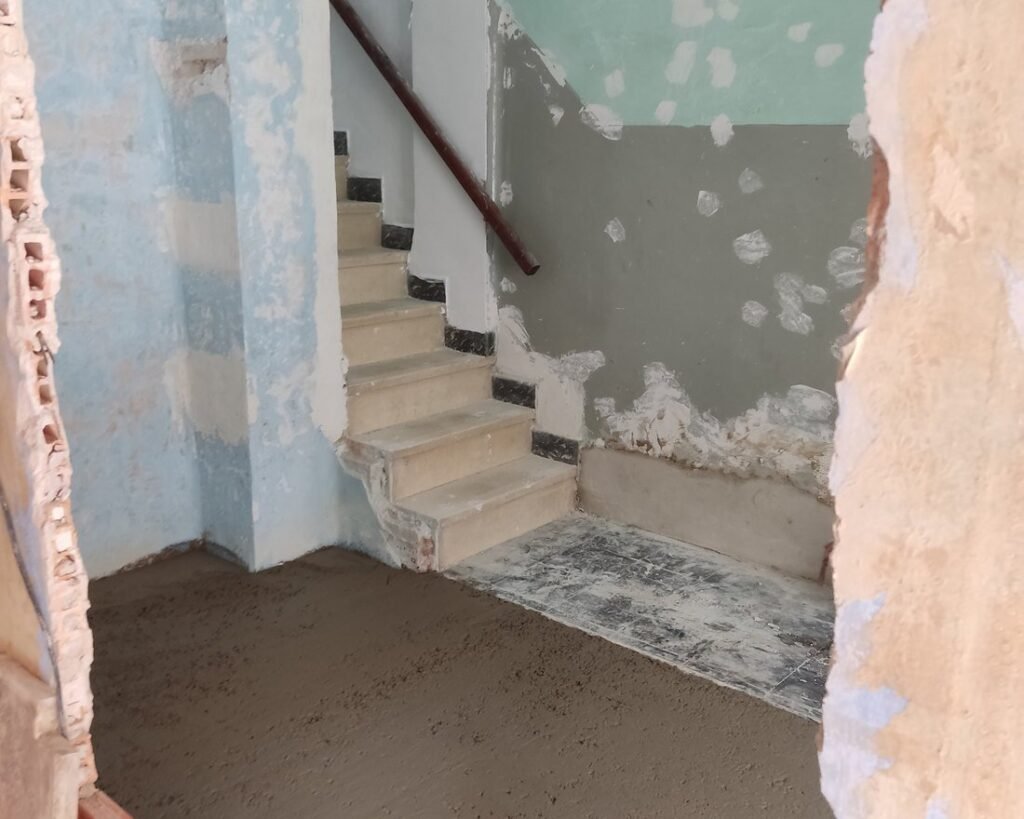 Entrada de una casa en obra, con las paredes picadas y el suelo en mortero