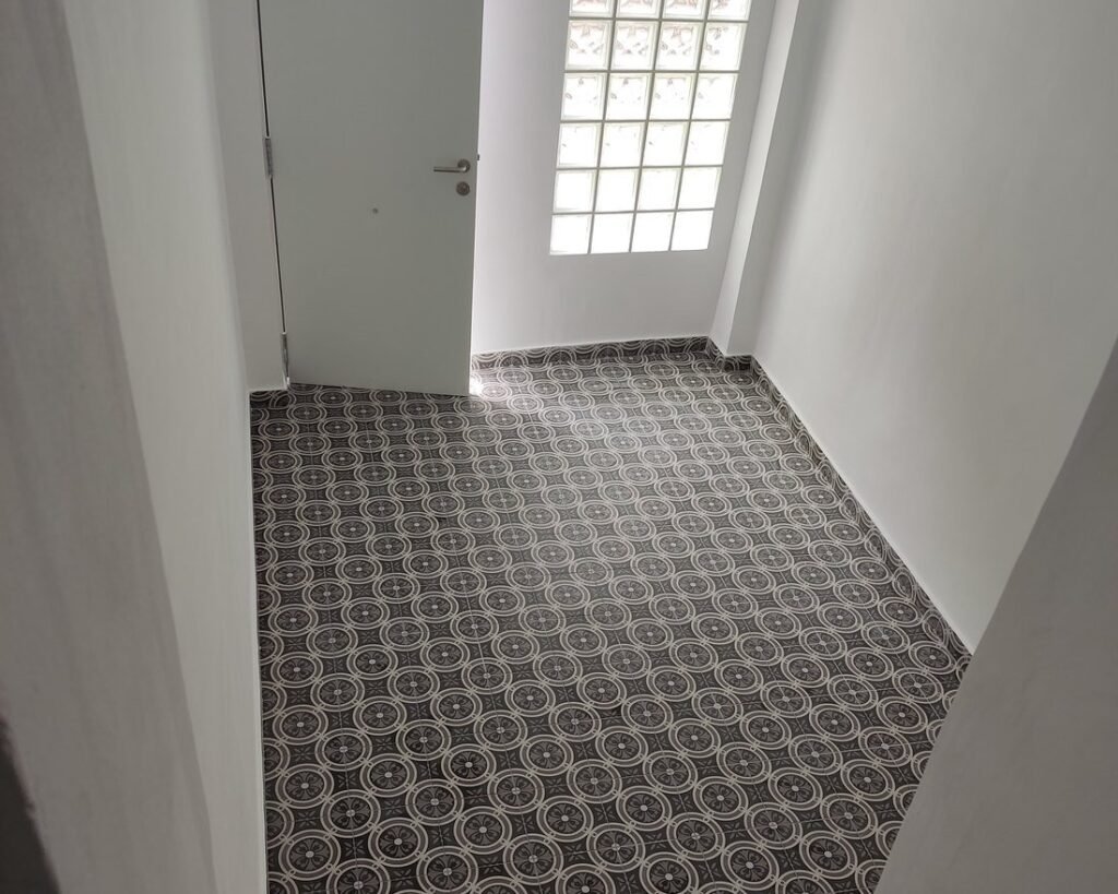 Entrada de una casa con suelo de baldosa estilo hidráulico, paredes enlucidas y ventana de pavés