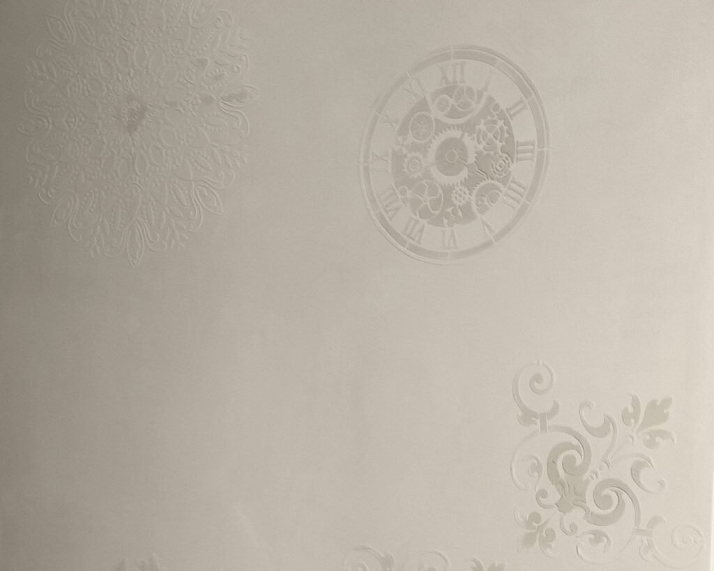 Pared de microcemento con relieves decorativos: mandala, reloj y volutas en blanco sobre blanco
