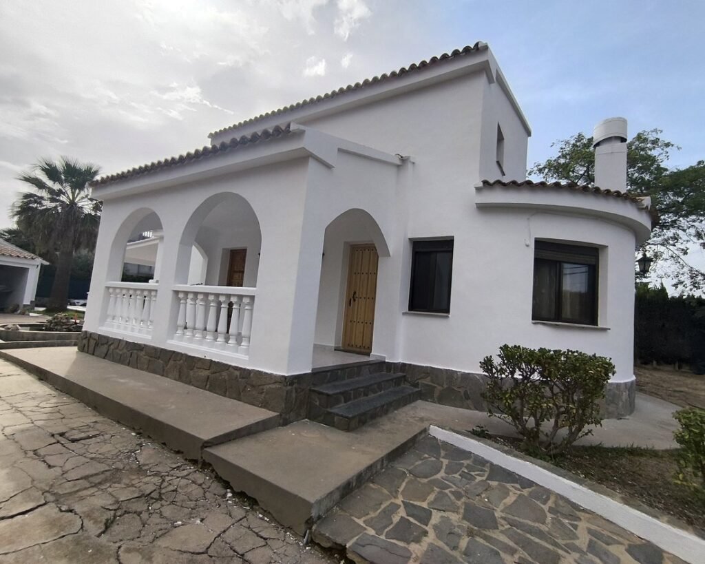 Chalet con la fachada exterior pintada en blanco, arcos y tejado de teja árabe