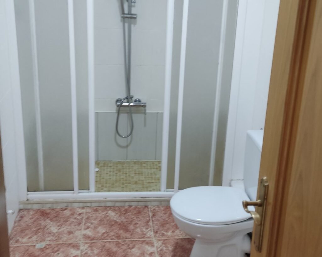 Baño con mampara corredera y suelo rosado, antes de la reforma