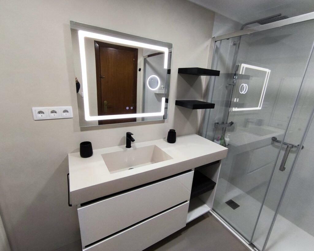 Baño reformado en microcemento, con espejo LED, mueble con lavabo integrado y mampara de cristal