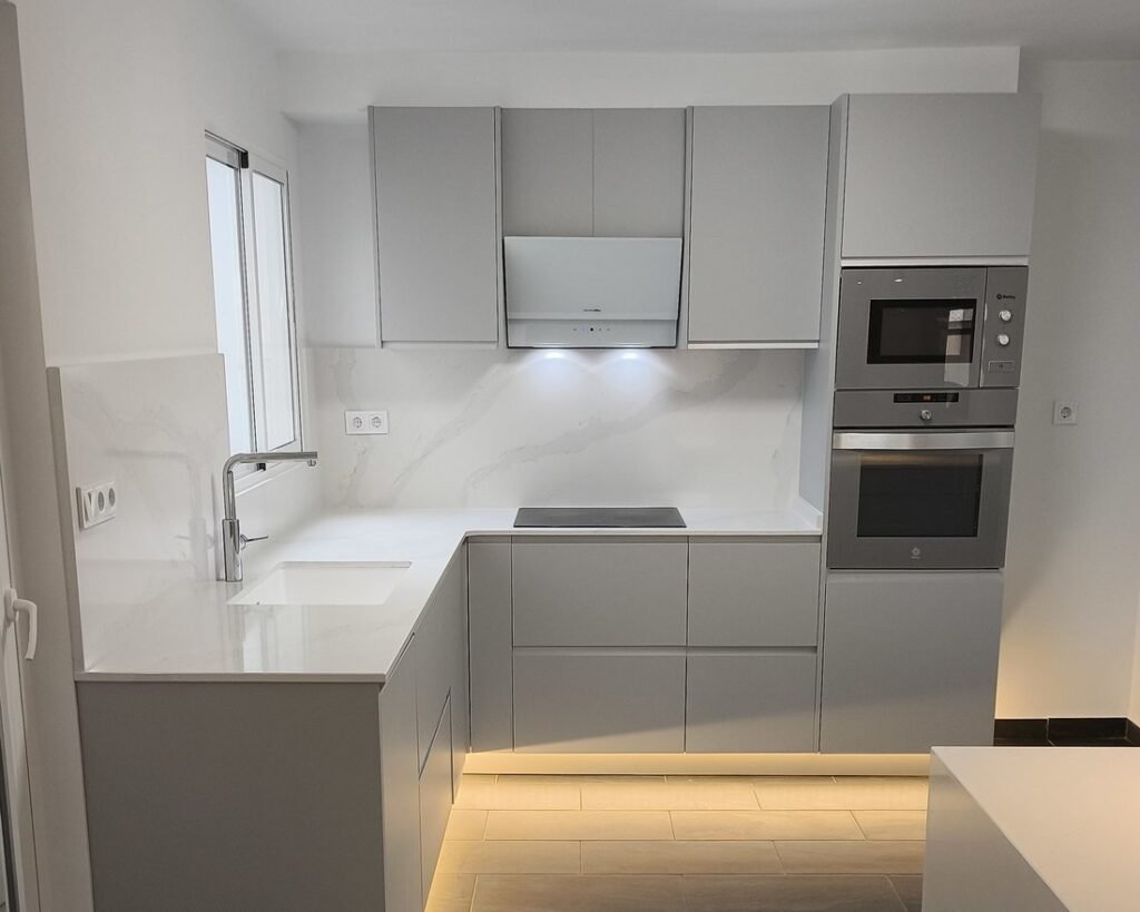 Cocina reformada con muebles gris claro, encimera tipo mármol y luz LED en el zócalo