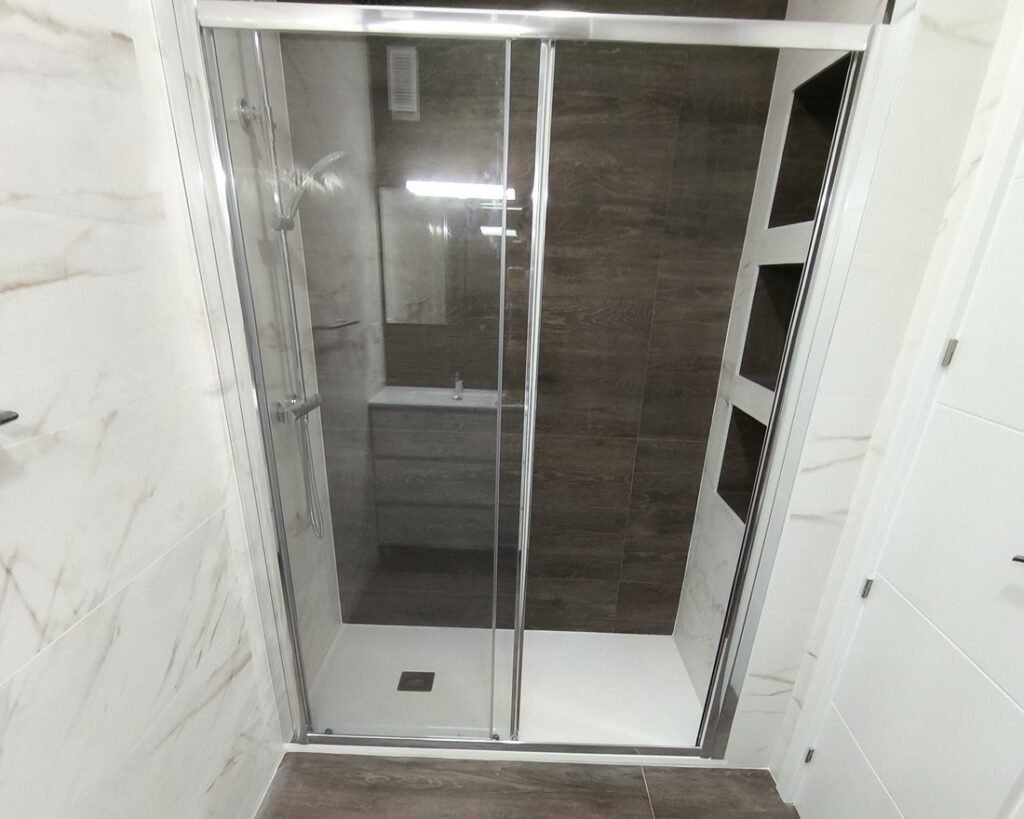 Baño de la vivienda de Silla con mampara corredera, pared efecto madera y azulejo tipo mármol
