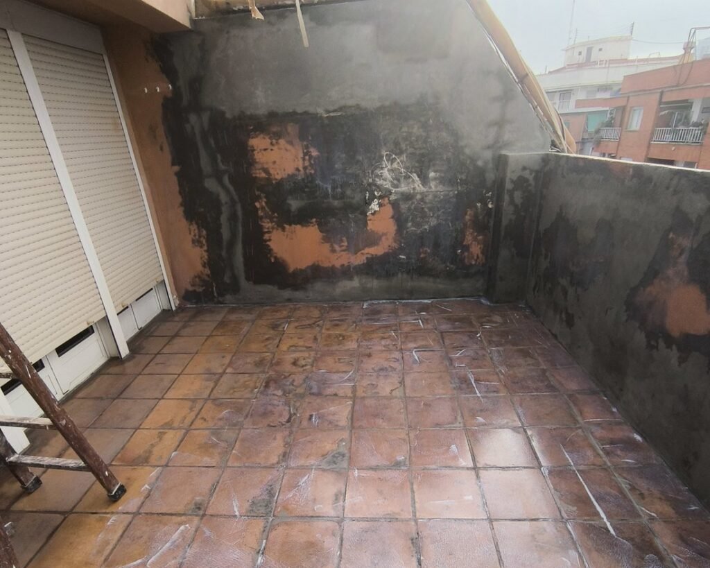 Terraza con la baldosa deteriorada y manchas de humedad en las paredes, antes de impermeabilizar