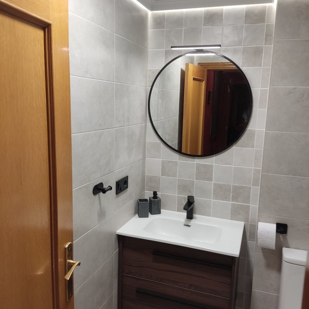 Lavabo del baño reformado en Carcaixent, con mueble de madera, espejo redondo y grifería negra