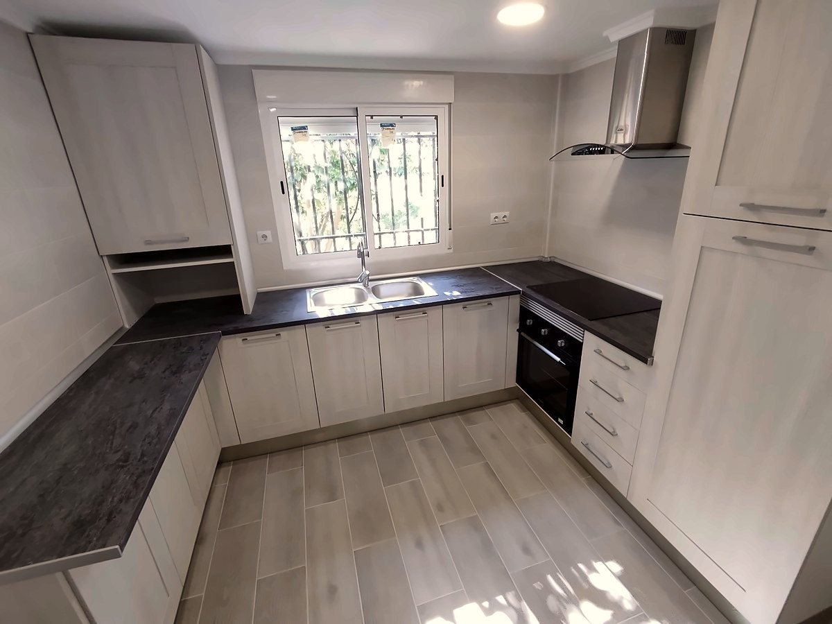 La misma cocina del chalet reformada, en L, con muebles claros y encimera oscura