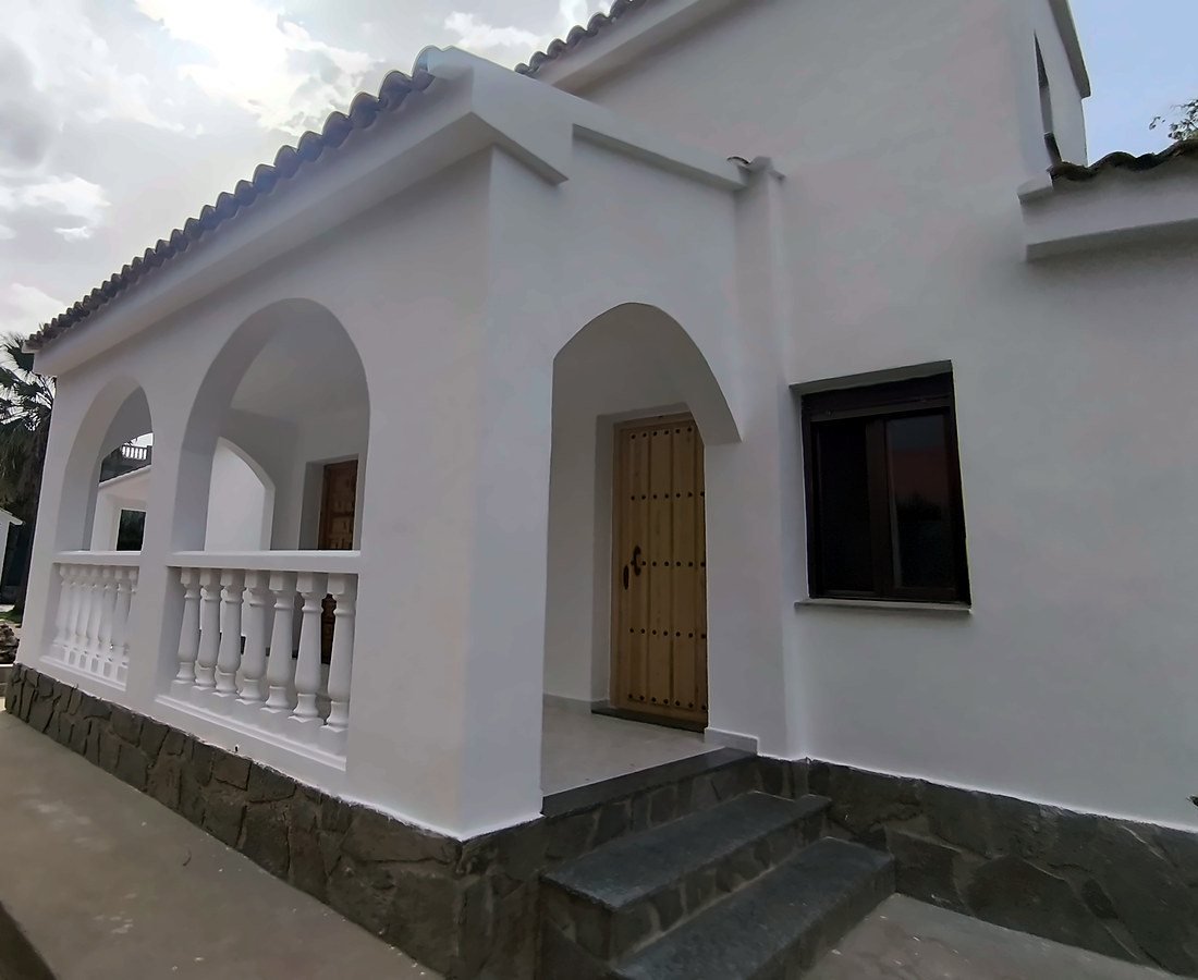 Chalet en Carcaixent con porche de arcos, balaustrada blanca y zócalo de piedra tras pintar la fachada
